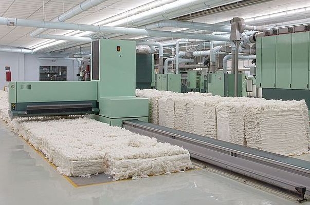 Initial stage of textile manufacturing, specifically the preparation of raw fibers for spinning